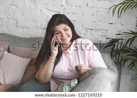 People, modern technology and communication concept. Picture of overweight stylish attractive young woman counsellor having consultation on positive body image using mobile phone, smiling happily
