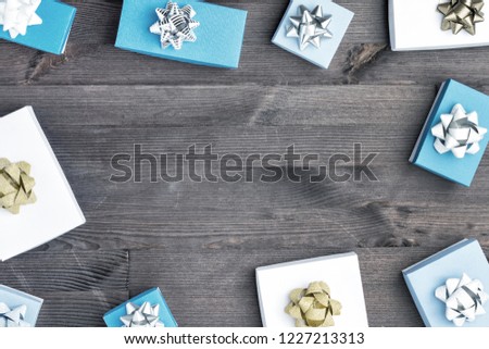 White and blue boxes are spread out in a circle on a brown wooden background. Gifts decorated with gold and silver bows. In the center is Copy Space. Holiday layout with space for text.