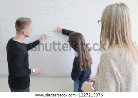 Two young college male and female students with young female teacher writting on the chalkboard during a math class.