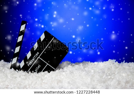 Frozen film clapper / clapperboard with falling snow on blue background with copy space