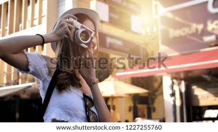 Beautiful young caucasian taking photos in city centre are walking Khaosan Road walking street in evening at Bangkok, Thailand. Happy female traveler and tourist concept.