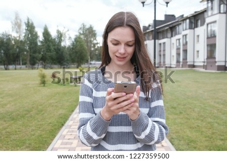 Beautiful brunette woman is reading something on mobile phone walking near the home.
