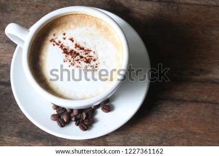 Cappuccino with milk froth and coffee beans on the old wooden desk as background.