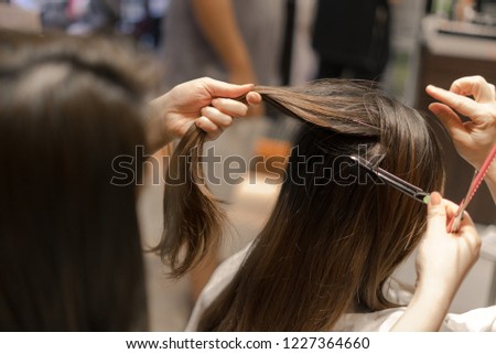 Hairdresser trimming black hair with scissors. Warm tone. Beauty salon. Royalty-Free Stock Photo #1227364660