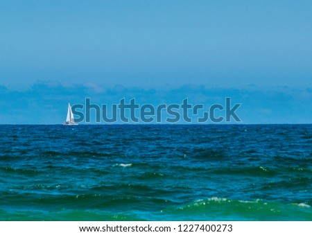 a distance photo of a white sloop sailing south along a calm ocean seen from the northern end of Sunshine Beach illuminated by the afternoon sunlight