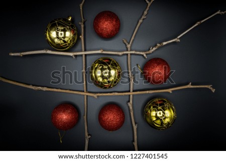 Tic-Tac-Toe game with dry branches and Christmas red and golden balls on black background.