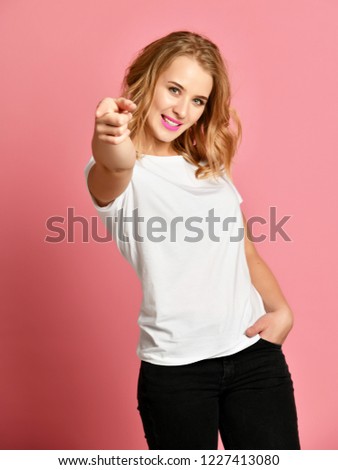 Beautiful woman in white t-shirt pointing finger at you with text space on pink background looking at the camera