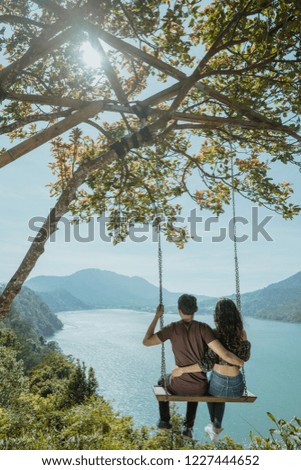 couple portrait enjoying nature on a hill top sitting on a swing together with the beautiful view in the background