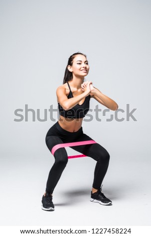 slim blonde woman doing squats with fitness loop band isolated on white background