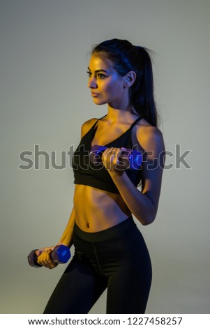 Full length portrait of sportswoman with strong body in tracksuit doing exercises with small weights isolated over purple background