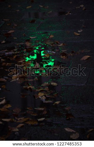 Reflection of pharmacy sign in water paddle in rainy autumn night. Slippery danger caution and first aid concept. Abstract background. Selective focus.
