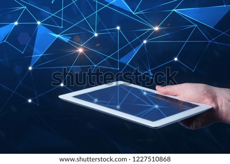 Hand of man holding tablet computer over dark blue background with glowing network hologram. Hi tech concept. Toned image