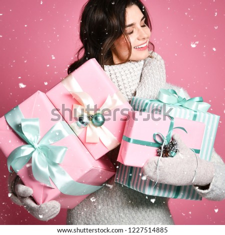 Cropped image of a smiling girl in grey sweater holding stack of gift boxes isolated over pink background. Xmas shopping