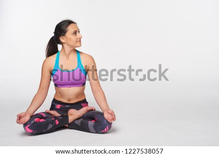 Young attractive woman practicing yoga, doing Padmasana, lotus pose in full length looking to side at blank copy space, isolated over white studio background
