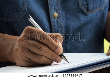 man's hand holding ballpoint pen writing on notebook.