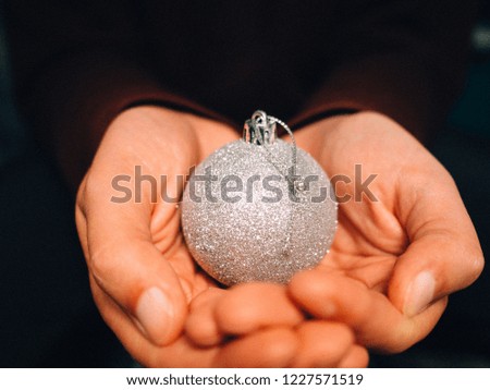 Hands holding a silver color Christmas ball.