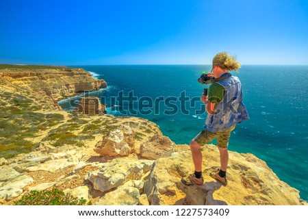 Travel photographer with stabilizer takes shot of Island Rock in Kalbarri National Park, Western Australia, in a sunny day with blue sky. Professional videomaker takes photo of Australian Coral Coast.