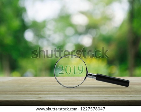 Magnifying glass with 2019 text and graph on wooden table over blur green tree in garden, Business happy new year research concept