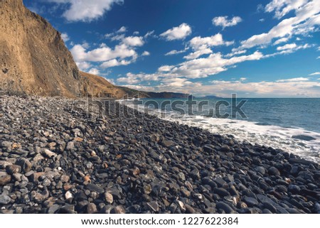 Stone coast with volcanic rocks in perspective with a horizon and blue sky.