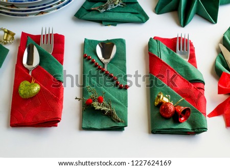 Christmas green and red colors paper napkins folded in various shapes on white surface with cutlery set and christmas decoration
