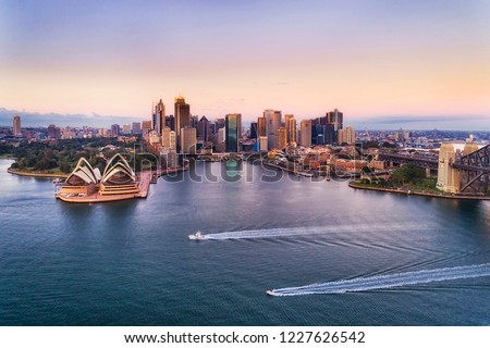 Two speed boats on calm waters of Sydney harbour in view of Circular quay and city CBD high-rise towers and Australian landmarks at sunrise with pink sky.