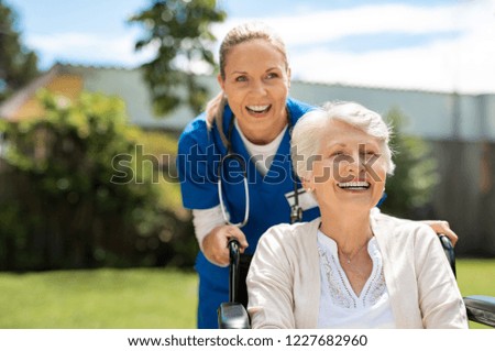 Happy nurse and elderly woman sitting in wheelchair enjoying outdoor. Beautiful nurse with laughing senior woman in wheelchair at outdoor park. Smiling disabled old lady in wheelchair at park.