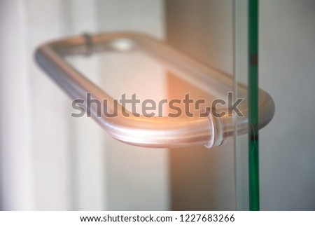 Silver Glass door handle of a glass partition shower unit. Bathroom glass door detail with bath tub in the background. Selective focus and soft light effect added.