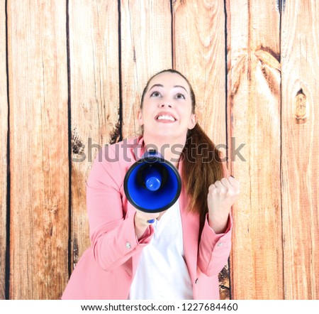 Excited young woman holding a blue megaphone against a wooden background