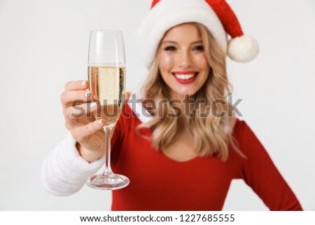 Portrait of a happy blonde woman dressed in red New Year costume standing isolated over white background, holding glass of champagne, celebrating