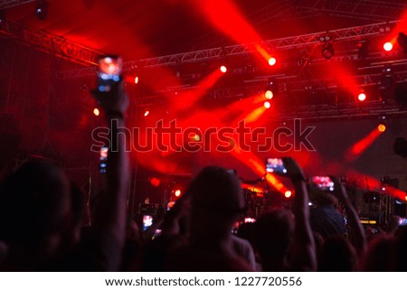 music scene with bright red spotlights and people near the stage with telephones taking pictures of the concert