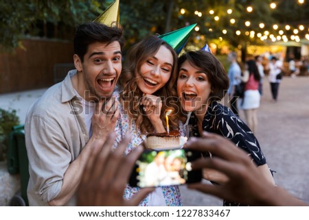 Group of laughing multhiethnic friends celebrating with a cake outdoors, taking picture with photo camera