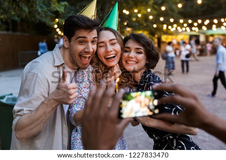 Group of happy multhiethnic friends celebrating with a cake outdoors, taking picture with photo camera