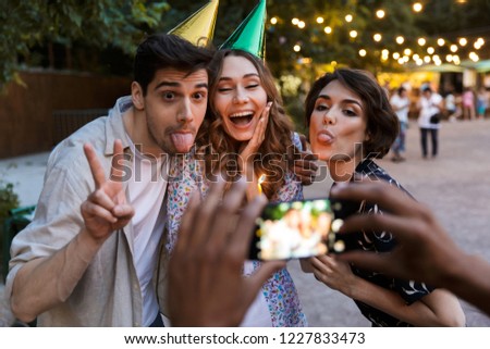 Group of cheerful multhiethnic friends celebrating with a cake outdoors, taking picture with photo camera