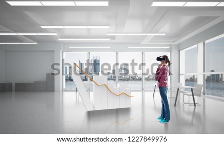 Young woman in casual wearing virtual helmet and working with graph. Mixed media