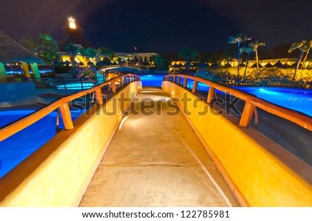 A bridge across swimming pool in a luxury caribbean resort at night, dawn time. Bahia Principe, Riviera Maya, Mexican Resort.