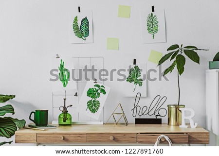 Stylish and modern scandinavian  home office desk with alot of floral graphics, avocado plant,cup of coffee and office accessories. Modern composition of home office desk.