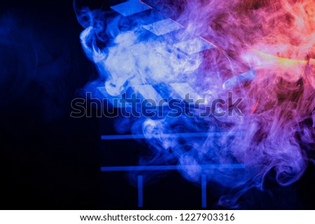 Black and white clapperboard for cinema close up among multicolored red and blue smoke in a man’s hand giving a command to start shooting on a black isolated background