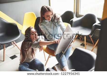 Two beautiful twin girls spend time read a book in library in the morning. Sisters relaxing in a cafe and having fun together.