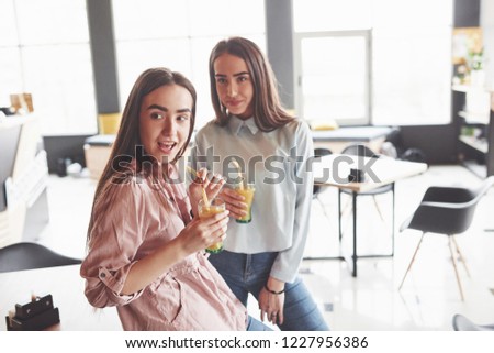 Two beautiful twin girls spend time drinking juice. Sisters relaxing in a cafe and having fun together.