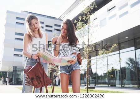 Young girls reading city map and looking for hotel. Lovely tourists with backpacks determine the concept of knowledge of the world.