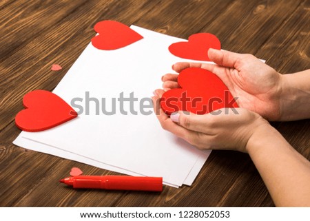 The girl paints her heart in a red, small brush, dark background. Preparing for the day of all lovers, Valentine's Day. background image