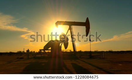 CLOSE UP: Industrial oil pump jack pumping crude oil for fossil fuel energy with drilling rig in oil field. Nodding donkey pump working over the setting sun in the middle of desert at golden sunset