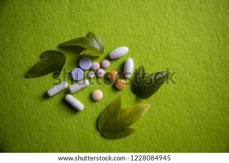 Pharmaceutical medicine pills, tablets and capsules in various colors on light spring green background with fresh green plant leaves. Nature. Top view. Helath care and pharmacy. Copy space for text. Royalty-Free Stock Photo #1228084945