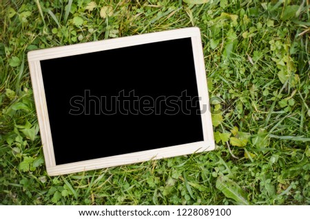 Frame with blank black background on green grass. The layout for the presentation. Mock up. empty wooden sign. Front view.