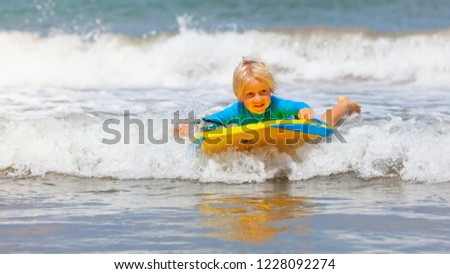 Happy baby boy - young surfer ride on surfboard with fun on sea waves. Active family lifestyle, kids outdoor water sport lessons and swimming activity in surf camp. Beach summer vacation with child.