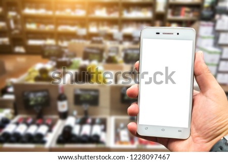 Men use hold smartphone blurred images of Various alcohol bottles in a row at the spirits store background.
