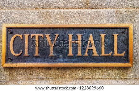 Exterior sign that reads "City Hall" in brass lettering. Graphic resource.