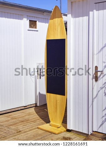 A blackboard shaped Surfboard on a beach white booths.