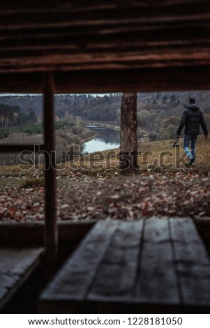 A man with camera go from landscape. Shoot from wooden room