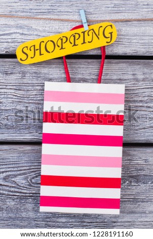 Colorful shopping bag on grey wooden background. Striped paper gift bag and yellow card with inscription shopping.